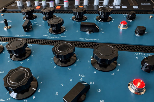Close-up of blue analogue equalizers with black controls and red indicator lights.